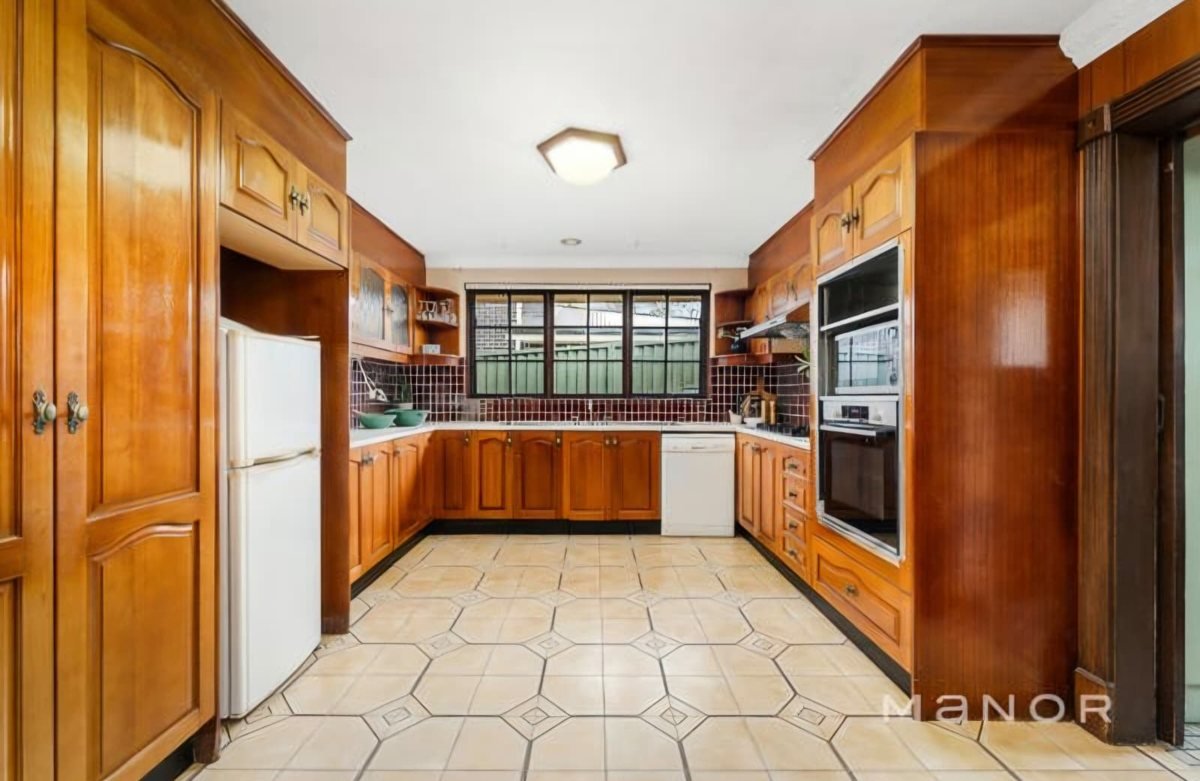 An older kitchen with orange timber cabinets and tiled floor, before its facelift