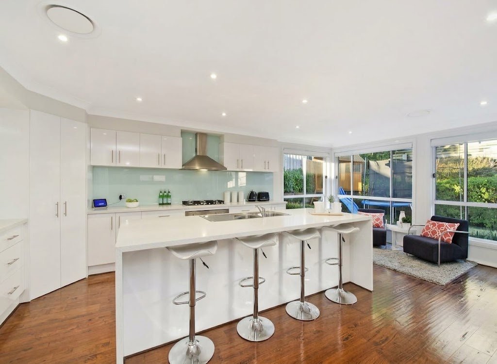 A modern kitchen with glossy white cabinets, a white island, bar stools and a pale green glass splashback