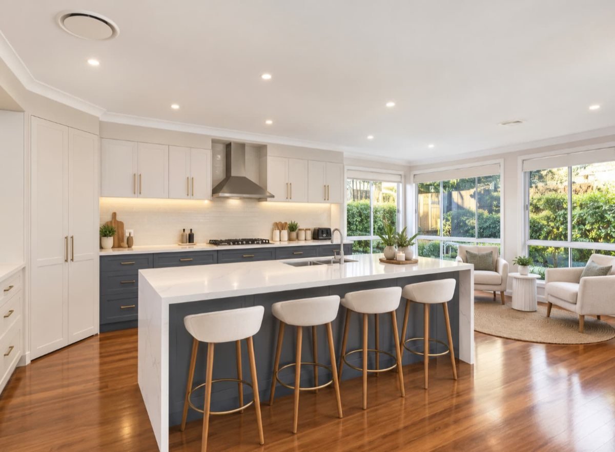 A finished open-plan kitchen with white cabinets, a navy island and a stone benchtop
